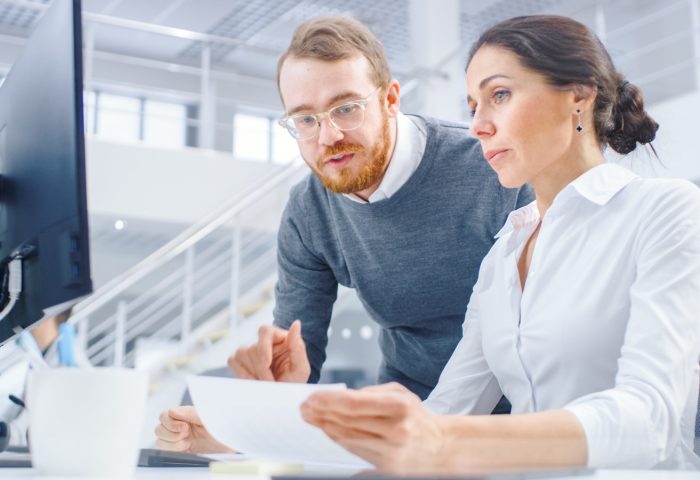 Businesswoman working at her desk with project manager standing beside her